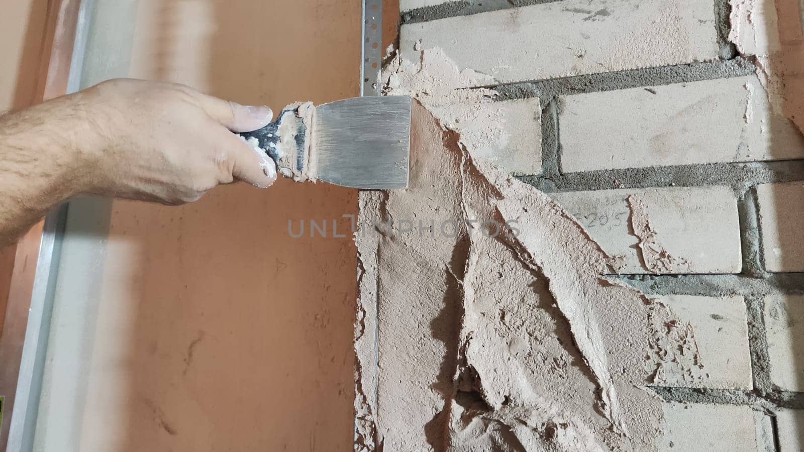 Close-up hand of man applying putty with a spatula. Home repair, decorative plaster on wall. Partial focus and blur for showing movement