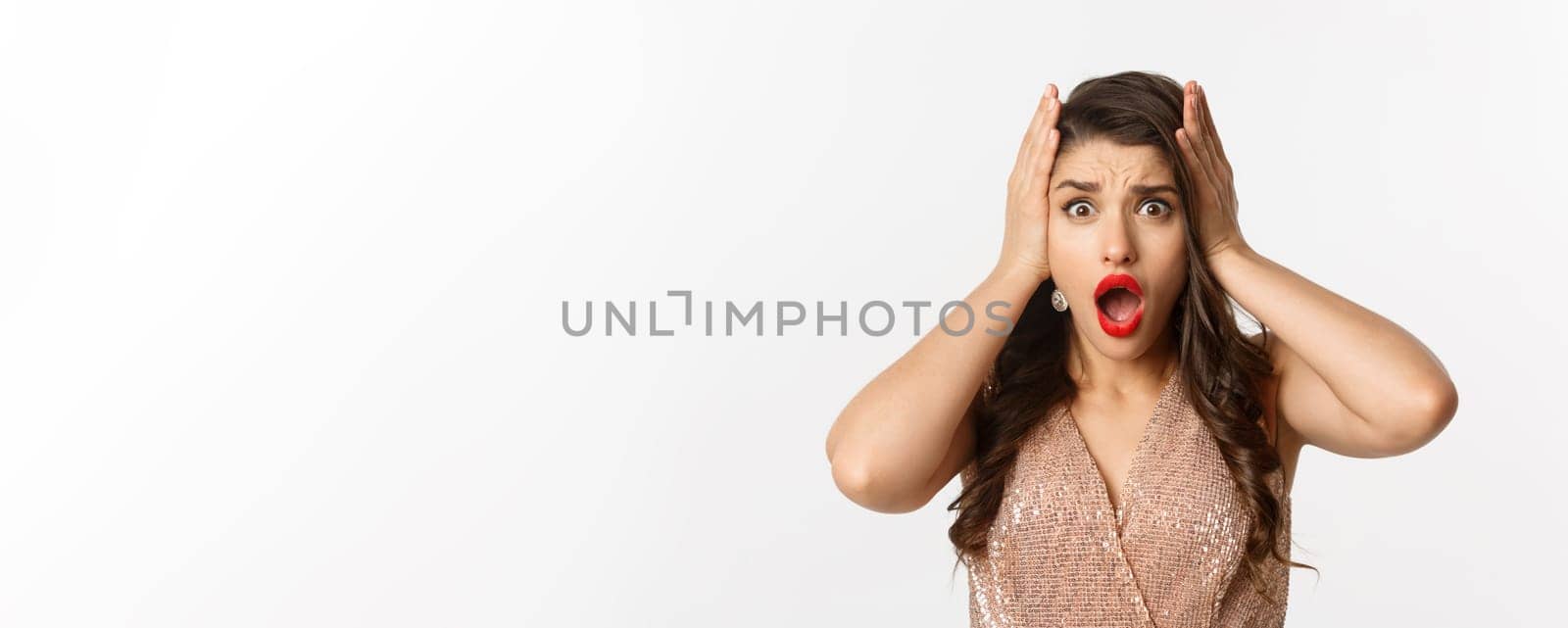 Concept of New Year celebration and winter holidays. Close-up of woman in luxury dress looking shocked and worried, standing over white background.