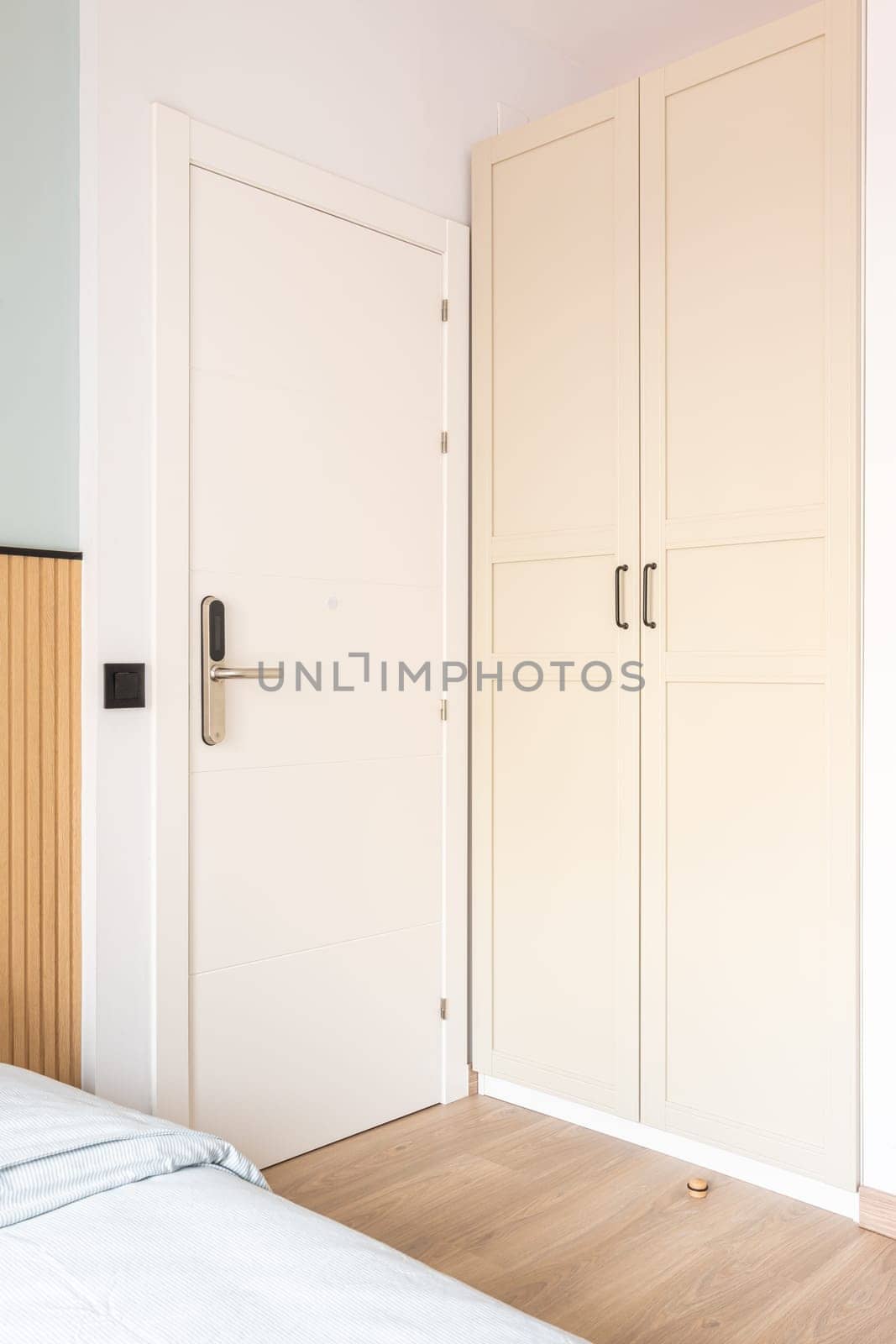 View of white front doors with electronic digital lock next to wardrobe and bed in hotel room. Concept of a modern security and protection system.