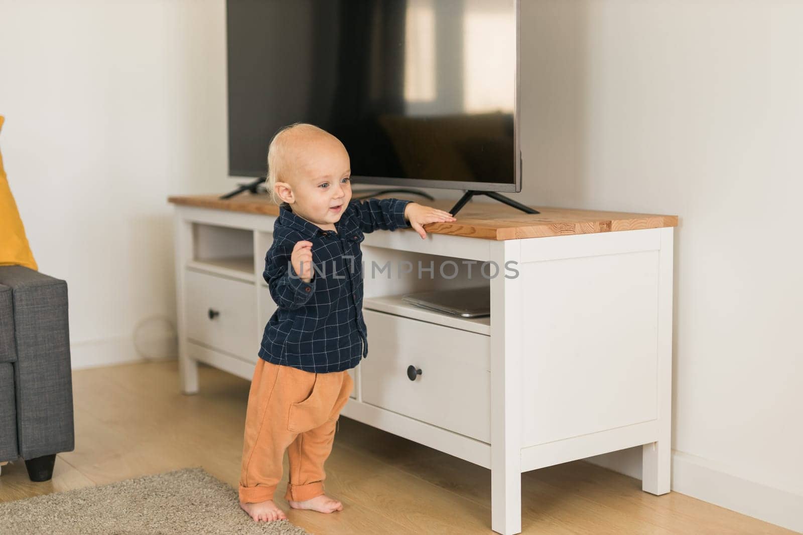 Toddler boy laughing having fun standing in living room at home copy space. Adorable baby making first steps alone. Happy childhood and child care concept by Satura86
