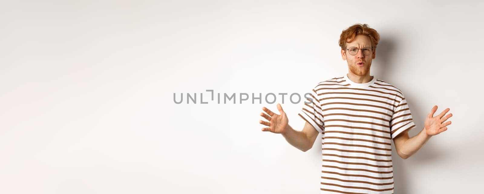 Impressed redhead man in glasses showing length of something big, demonstrate large size and looking amazed, standing over white background by Benzoix