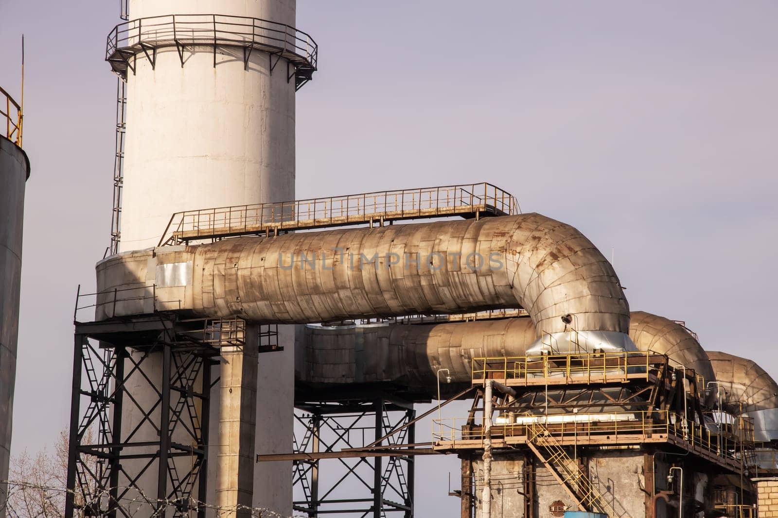 Large plant pipes and ladders on blue sky background close up