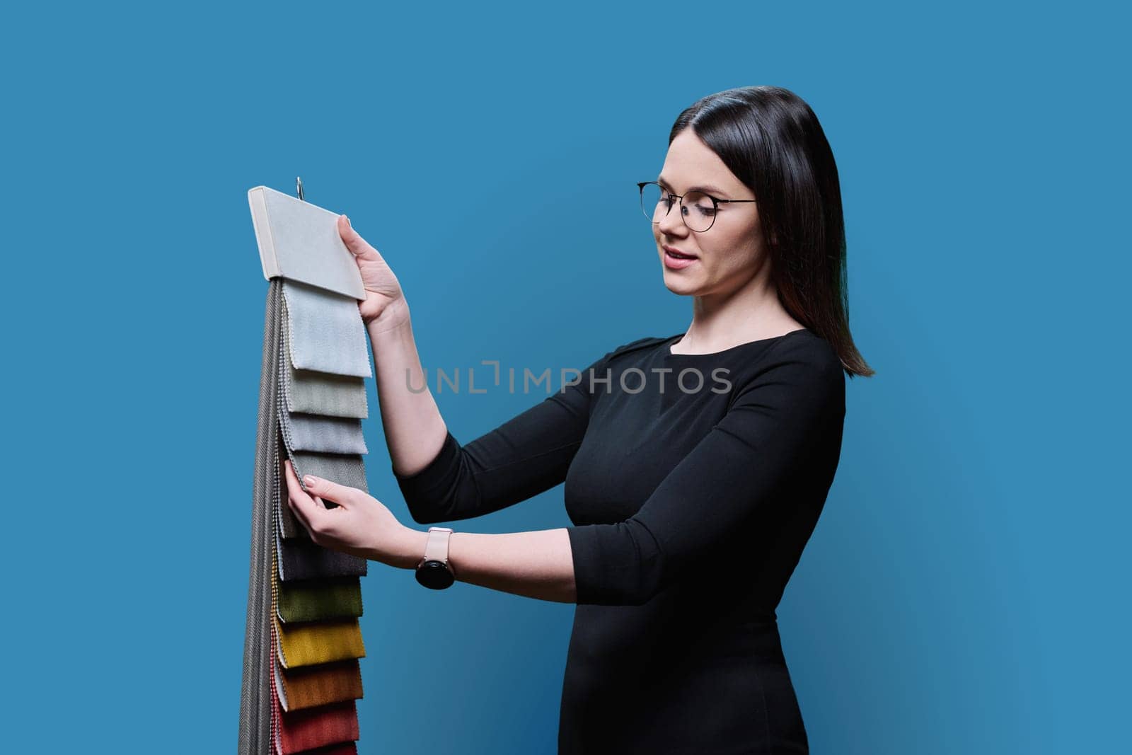 Young woman choosing decorative fabrics for interior, on blue color studio background. Female with hanger color palette of trendy upholstery fabric for furniture curtains, renovation new home concept