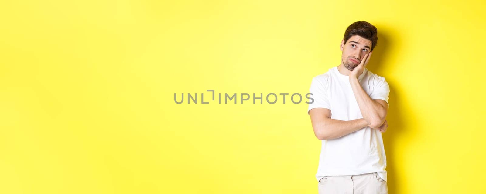 Bored and gloomy guy looking up, imaging things, standing over yellow background by Benzoix