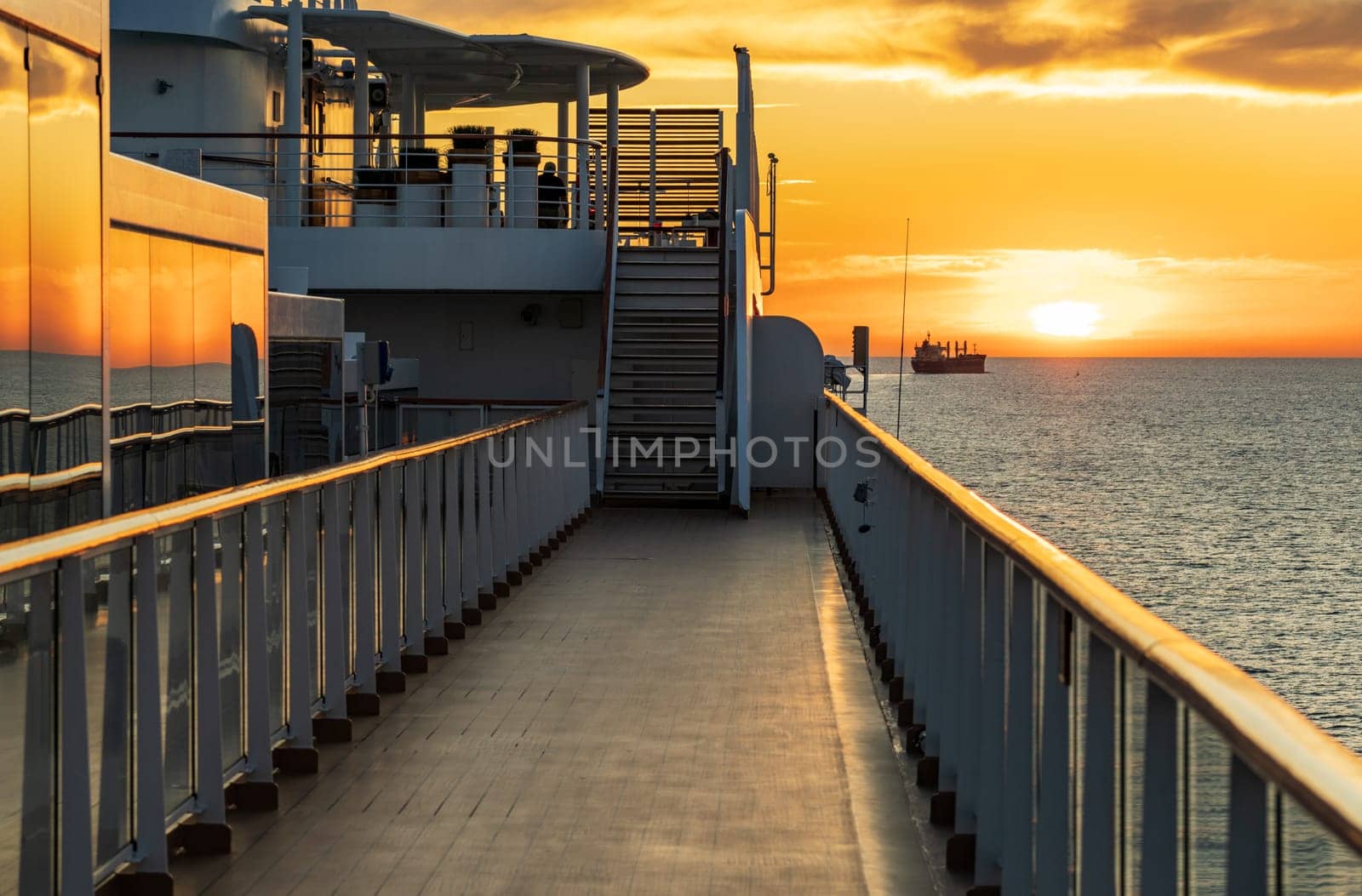 Sun setting over the water horizon with a cruise ship in the foreground and bulk carrier cargo ship behind