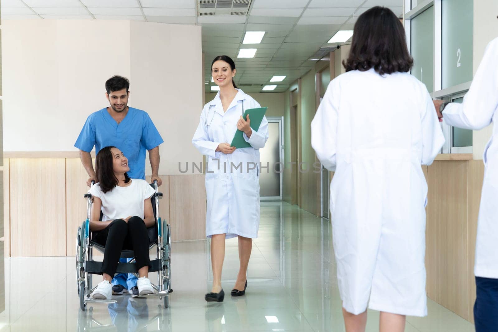 Doctor and nurse transport female patient in wheelchair at sterile corridor. by biancoblue