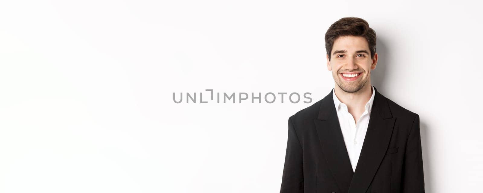 Close-up of handsome young businessman in trendy suit smiling, standing against white background by Benzoix