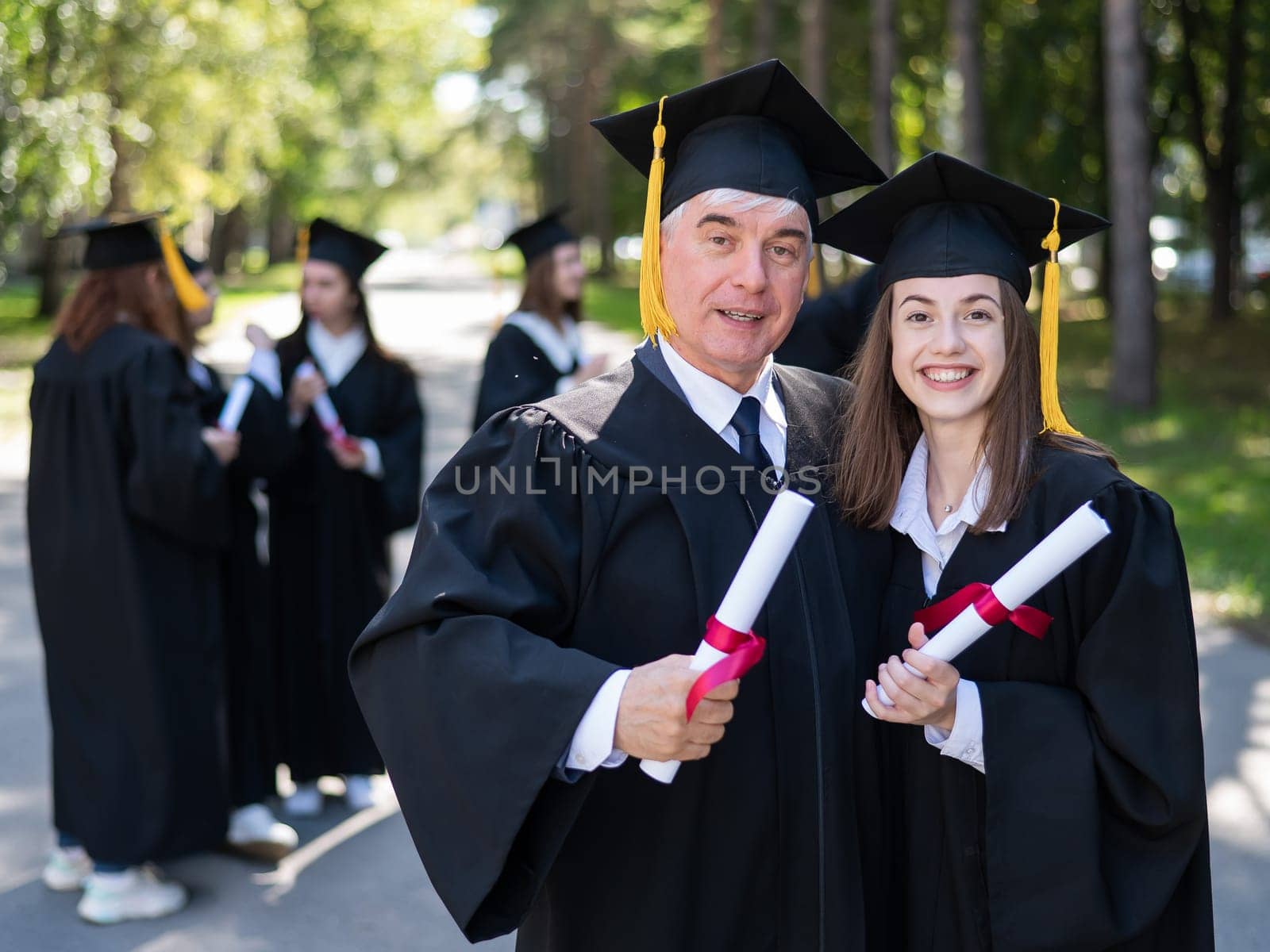 A group of graduates in robes outdoors. An elderly man and a young woman congratulate each other on their graduation. by mrwed54