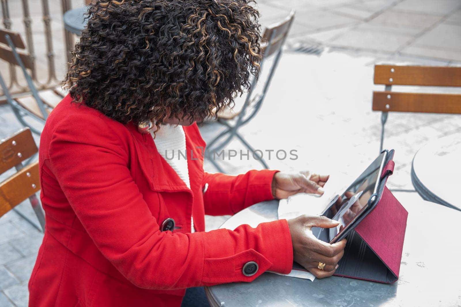 a young african american woman in a red coat sits at a table in a cafe and checking bill after shopping using a tablet, financial problems crisis, proper planning of expenses, High quality photo