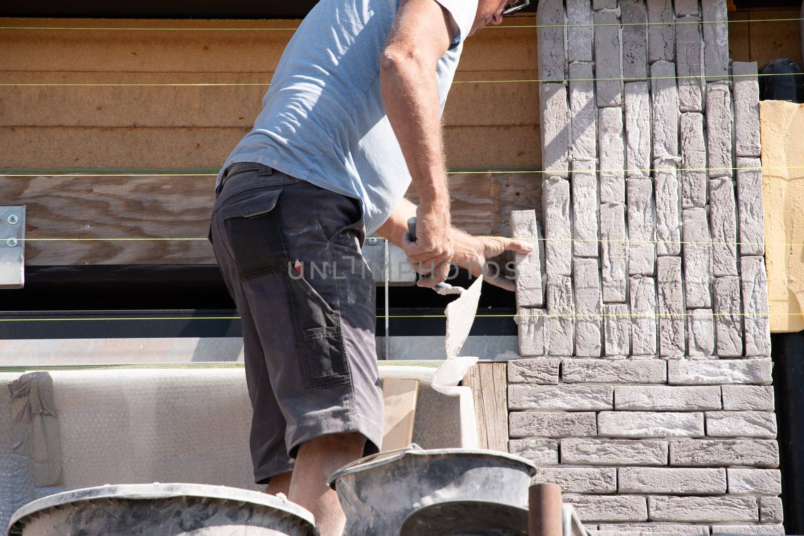 masonry worker the bricklayer makes the facade of the house from gray bricks by KaterinaDalemans