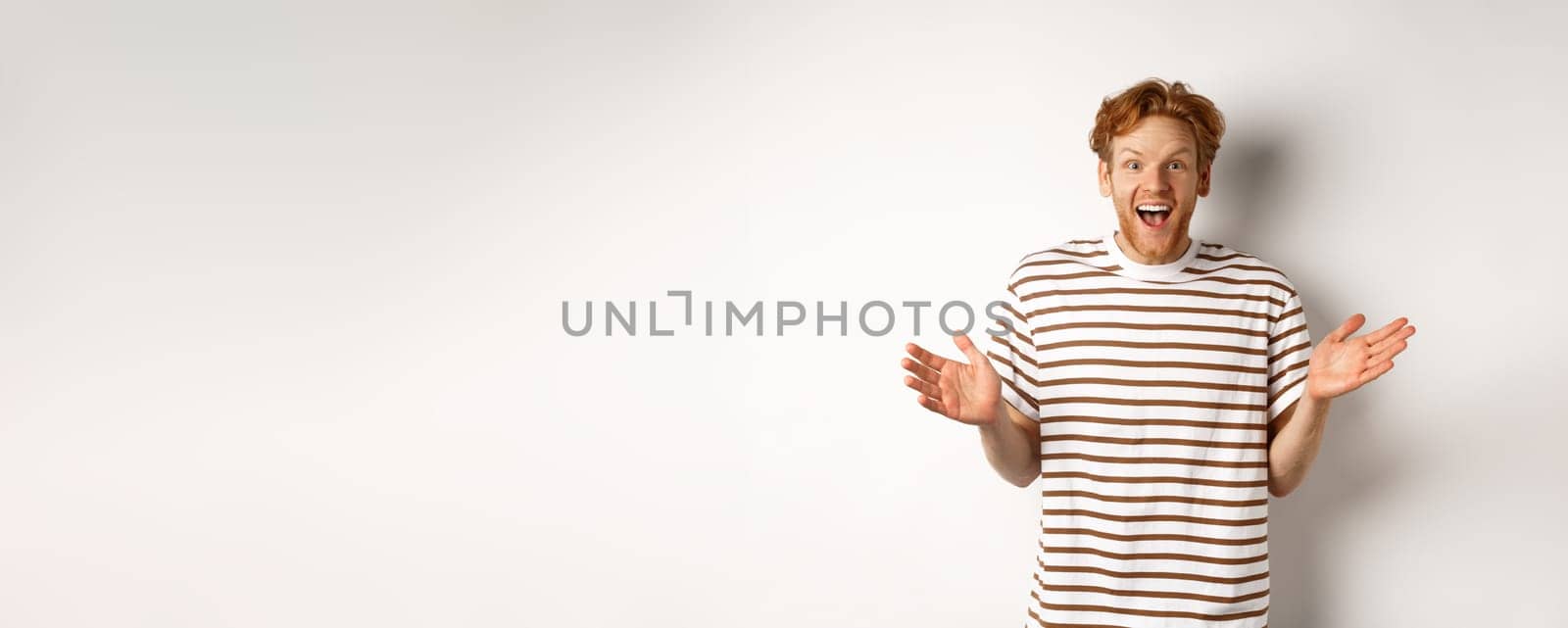 Happy and surprised redhead man rejoicing of good news, looking amazed and pleased at camera, white background.