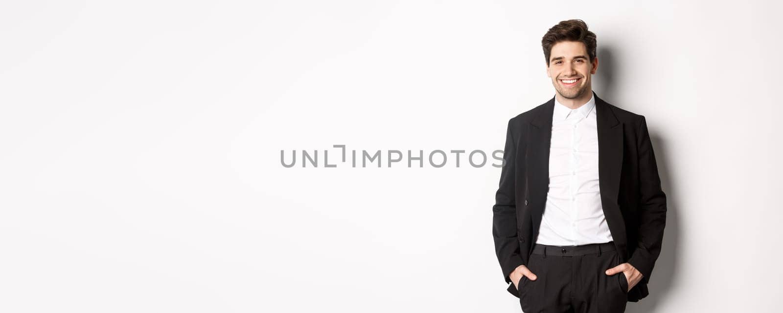 Image of handsome caucasian man in party suit, smiling pleased, attend formal event, standing over white background.