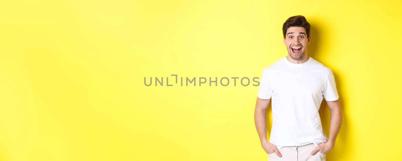 Man looking surprised, smiling amazed and looking at announcement, standing near copy space, yellow background by Benzoix