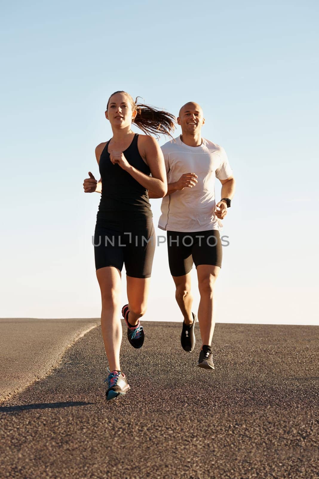 Going the distance together. a young couple exercising outdoors. by YuriArcurs