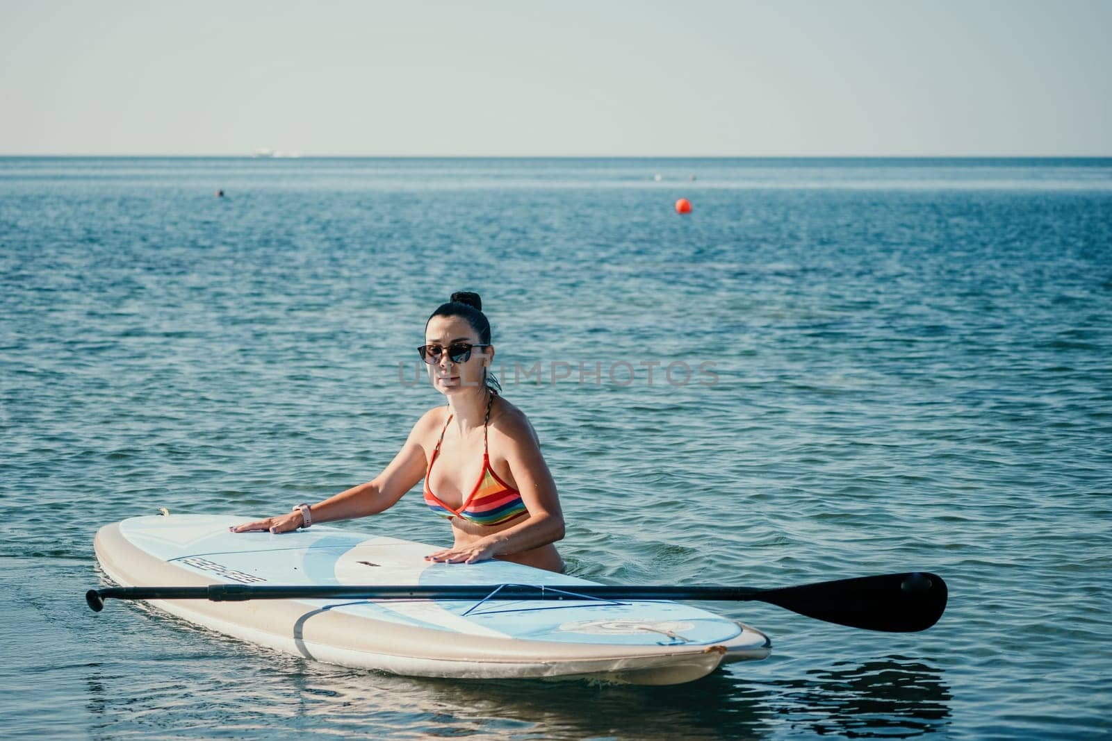 Sea woman sup. Silhouette of happy middle aged woman in rainbow bikini, surfing on SUP board, confident paddling through water surface. Idyllic sunset. Active lifestyle at sea or river