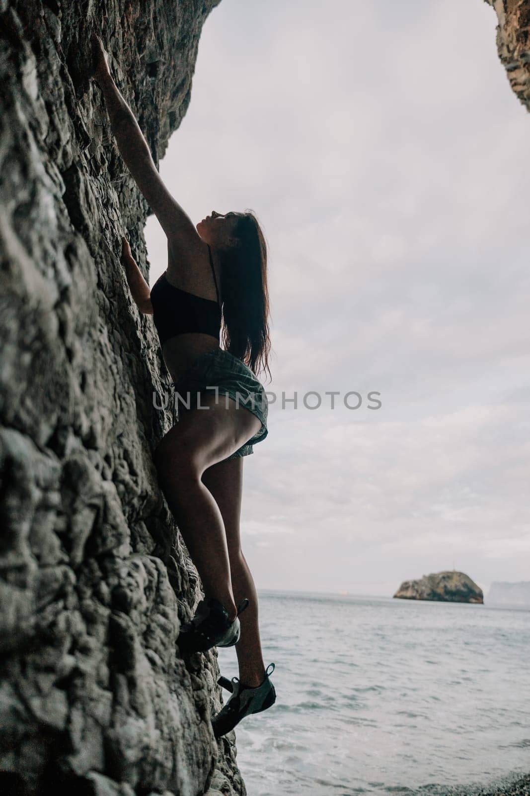 A girl climbs a rock. The athlete trains in nature. Woman overcomes difficult climbing route. Extreme hobby. Tourist woman rock climber hiking on mountains rocks over beautiful sea coast