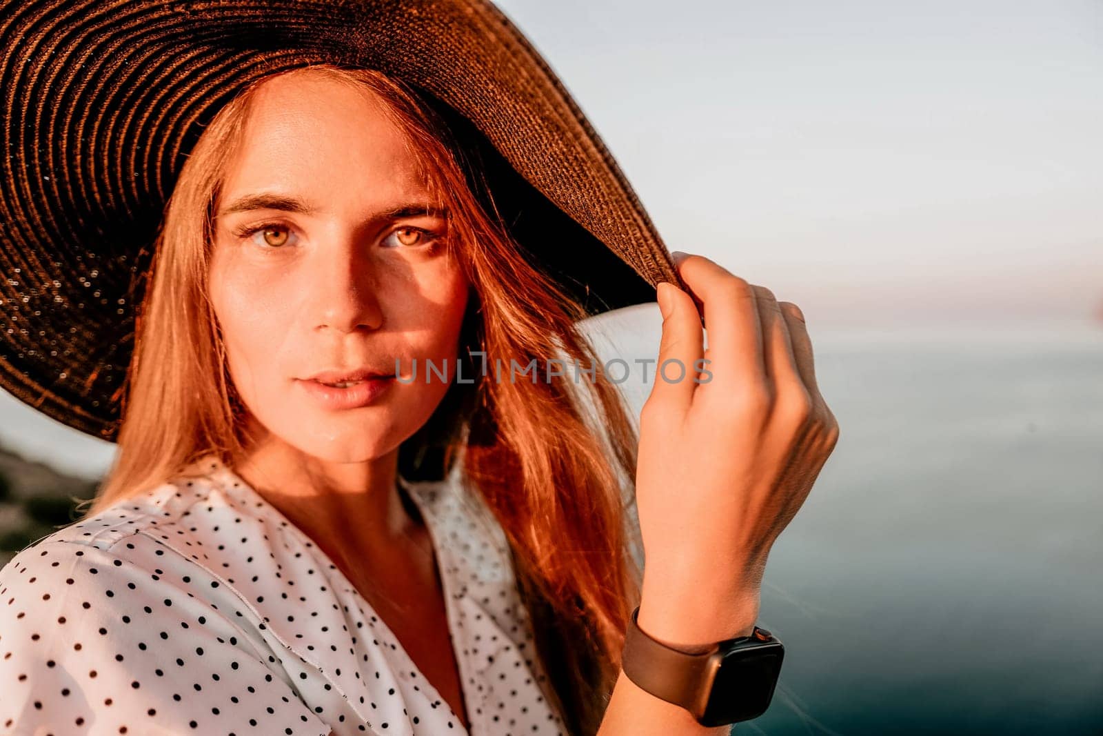 Portrait of happy young woman wearing summer black hat with large brim at beach on sunset. Closeup face of attractive girl with black straw hat. Happy young woman smiling and looking at camera at sea. by panophotograph