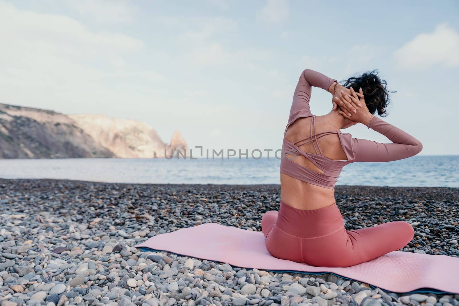 Middle aged well looking woman with black hair doing Pilates with the ring on the yoga mat near the sea on the pebble beach. Female fitness yoga concept. Healthy lifestyle, harmony and meditation.