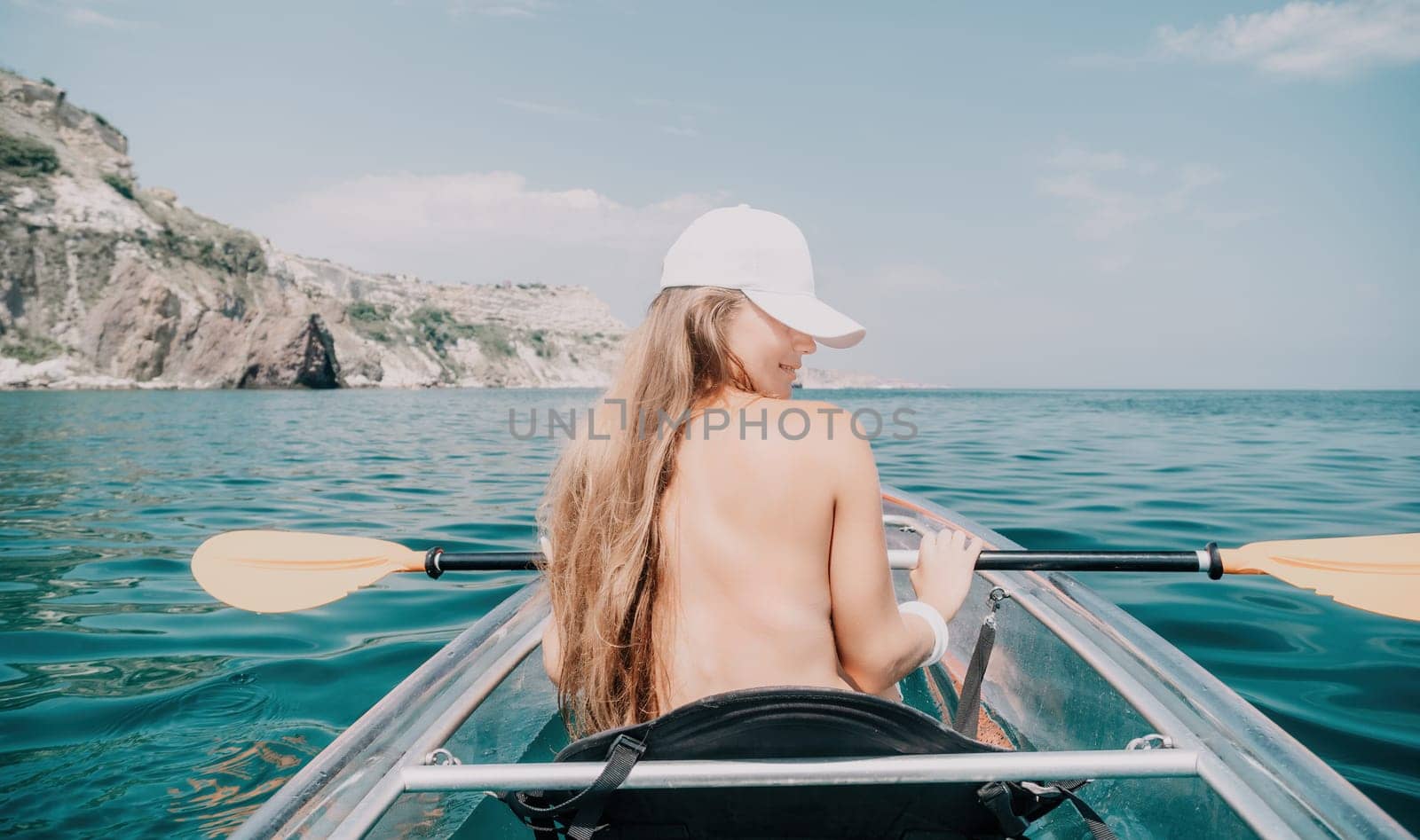 Woman in kayak back view. Happy young woman with long hair floating in transparent kayak on the crystal clear sea. Summer holiday vacation and cheerful female people having fun on the boat.