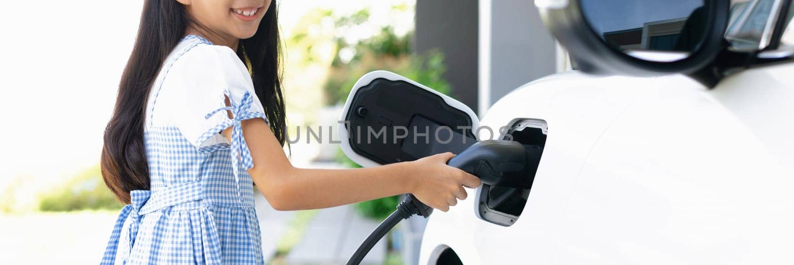 A playful girl holding an EV plug, a home charging station providing a sustainable power source for electric vehicles. Alternative energy for progressive lifestyle.