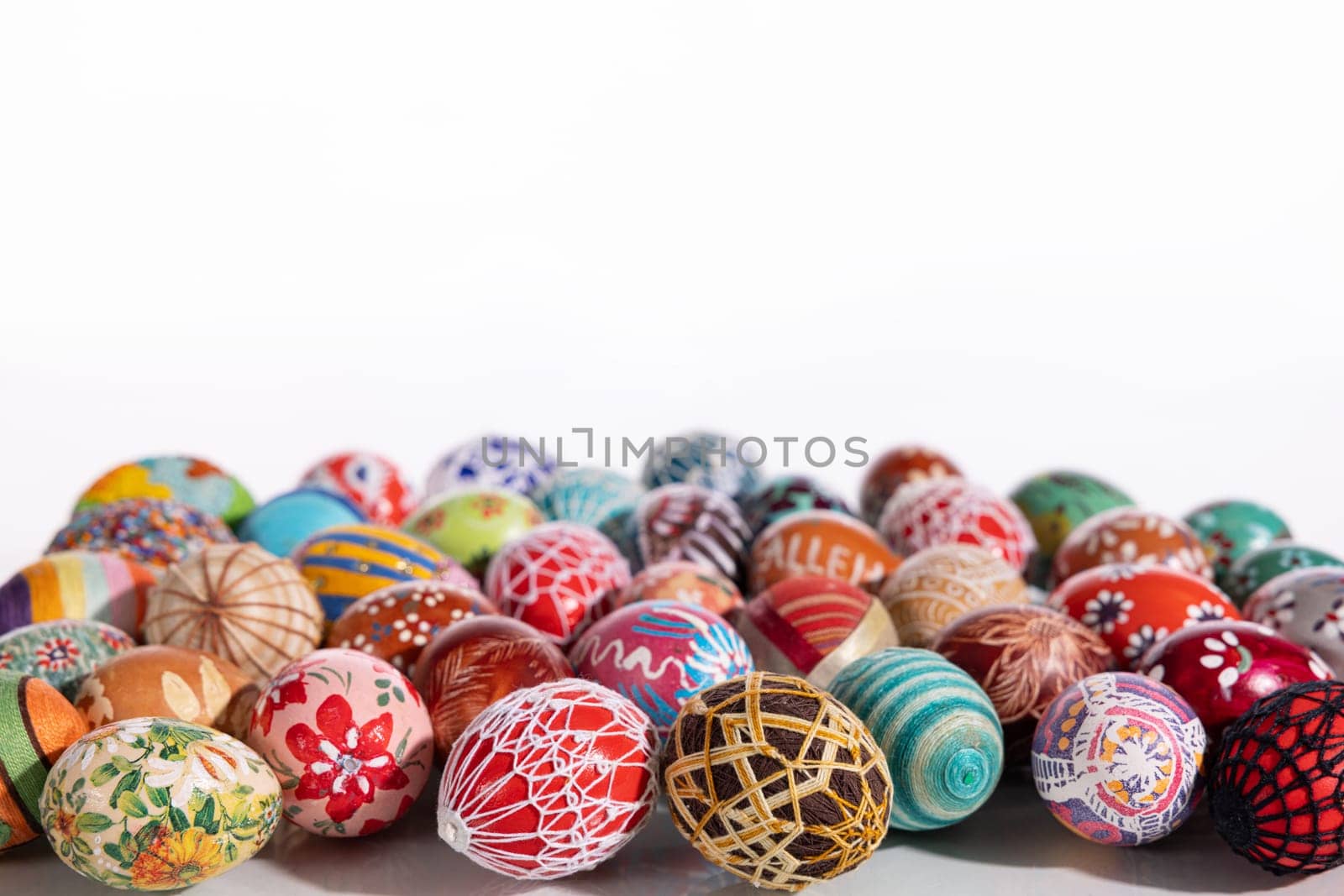 Easter eggs made in different technologies and arranged on a white background in rather random places. A large number of colorful eggs lying side by side.