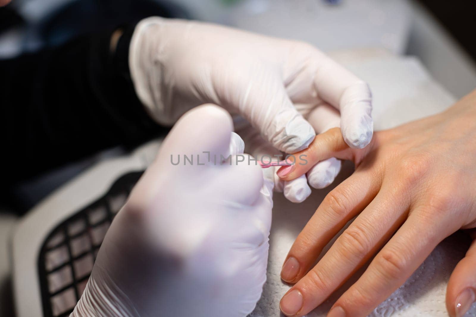 Performing hybrid manicure on natural nail plate. A beauty salon client experiences a hybrid manicure service.