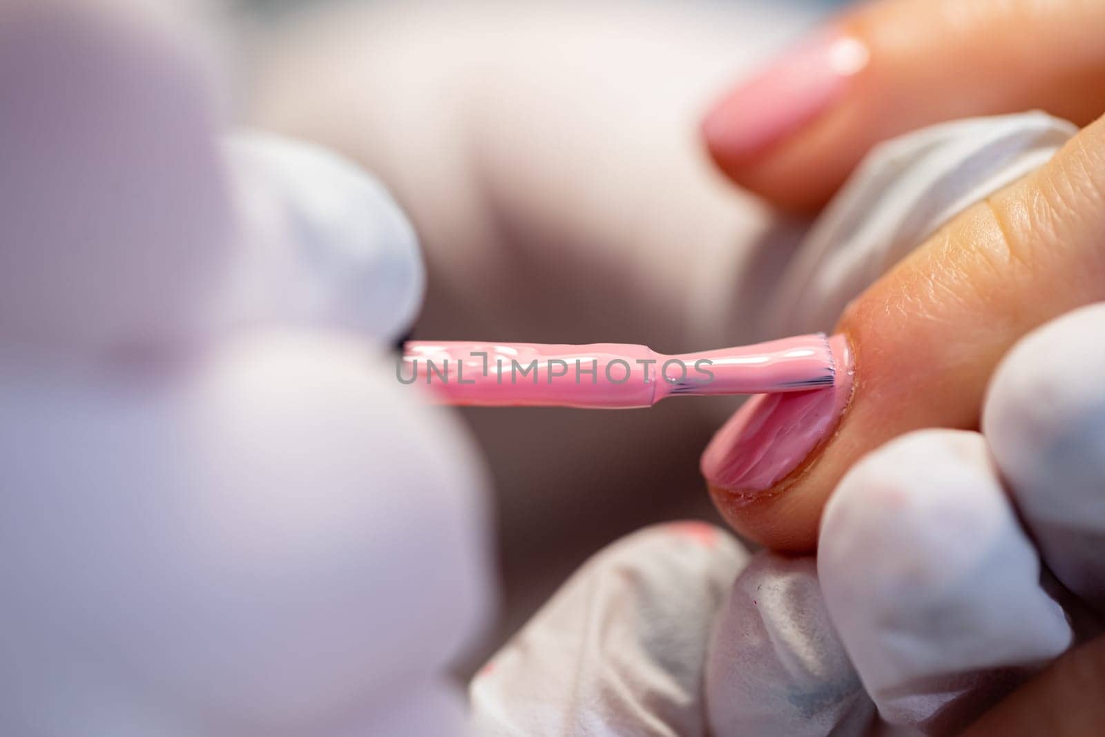 Large close-up of a brush covered with pink nail polish. Blurred foreground. The finger of a beauty salon customer seen in high magnification. Painting nails in pink.