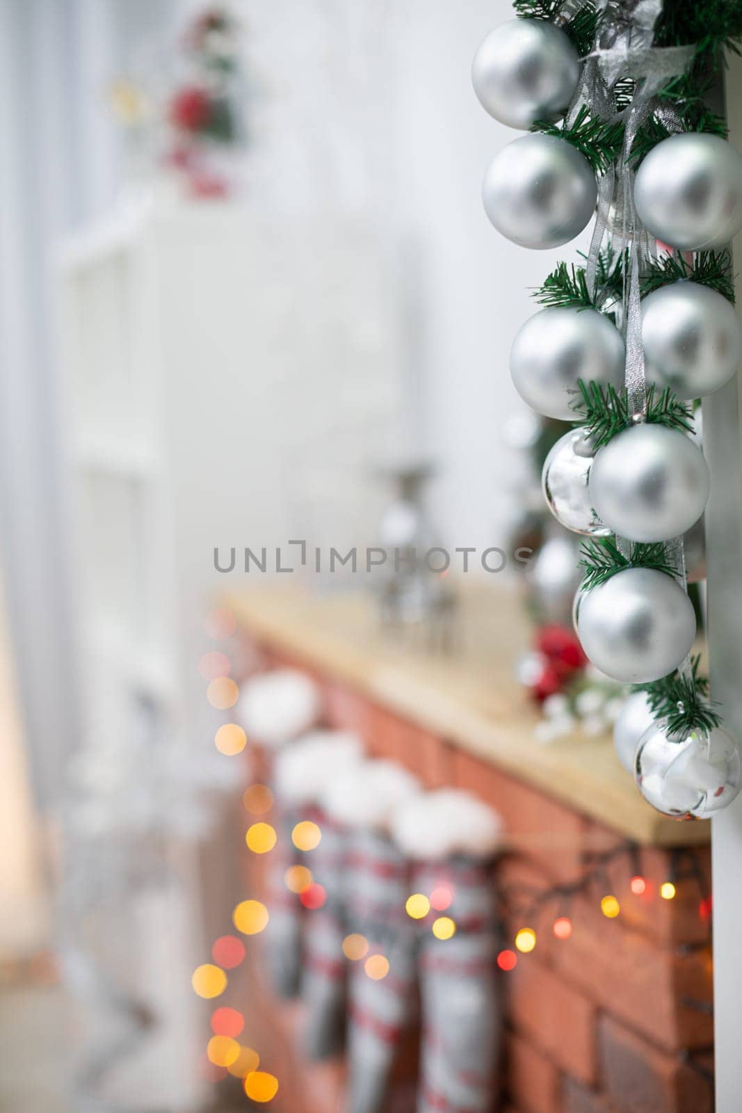 Silver baubles on spruce twigs and decorated fireplace in background.