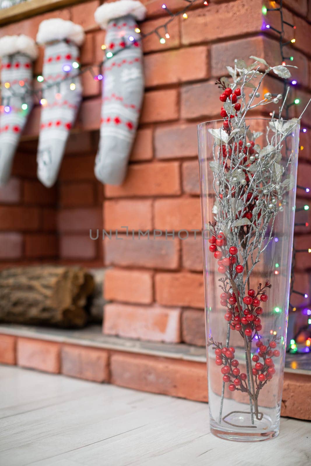 A brick fireplace and a glass vase with decorations and Christmas lights and socks as decorations for Christmas.