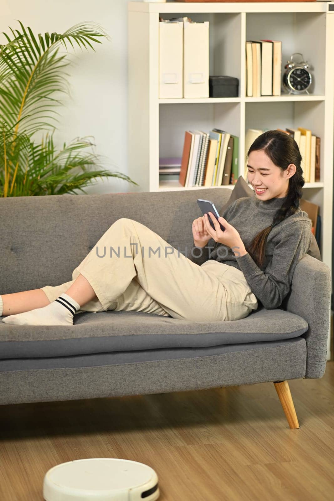 Happy young woman relaxing on couch and chatting online on mobile phone. People, technology and lifestyle concept.