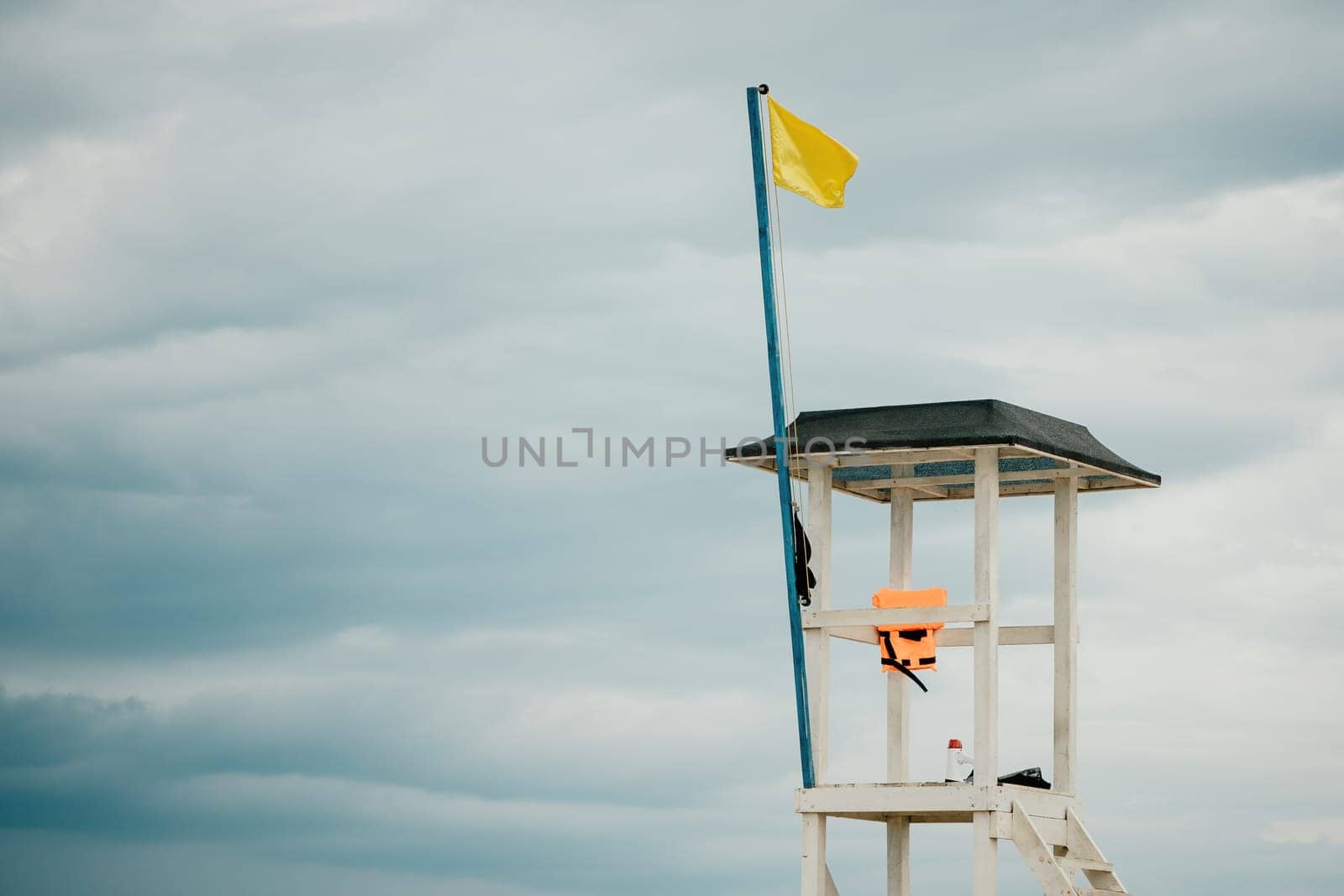 Empty white lifeguard tower with a yellow flag on the beach in windy weather. Beach lifeguard tower with yellow flag indicator. Nobody. Holiday recreation concept