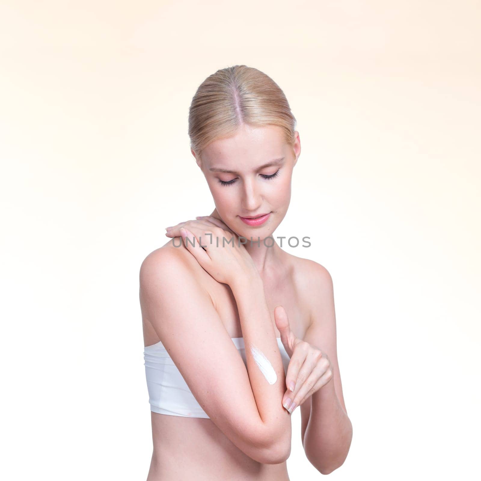 Personable beautiful woman putting skincare moisturizer cream on her arm looking in camera in isolated background as concept for beauty care treatment. Female model applying lotion on her body.