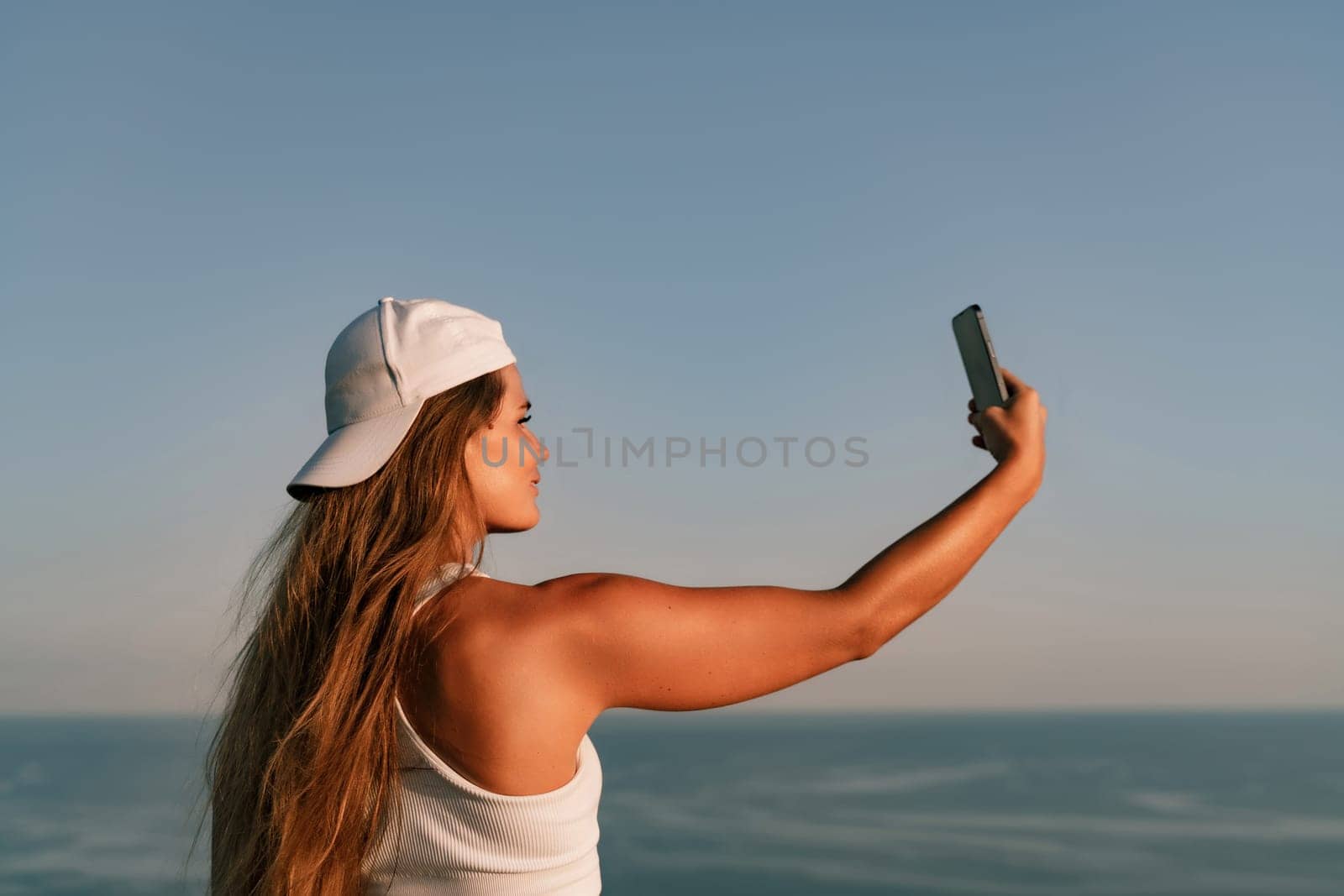 Selfie woman in cap and tank top making selfie shot mobile phone post photo social network outdoors on sea background beach people vacation lifestyle travel concept. by Matiunina