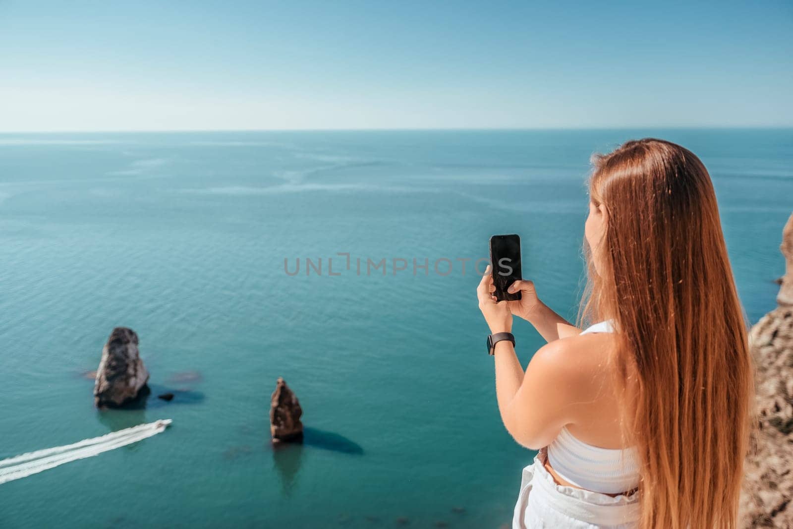 Successful business woman in yellow hat working on laptop by the sea. Pretty lady typing on computer at summer day outdoors. Freelance, travel and holidays concept.