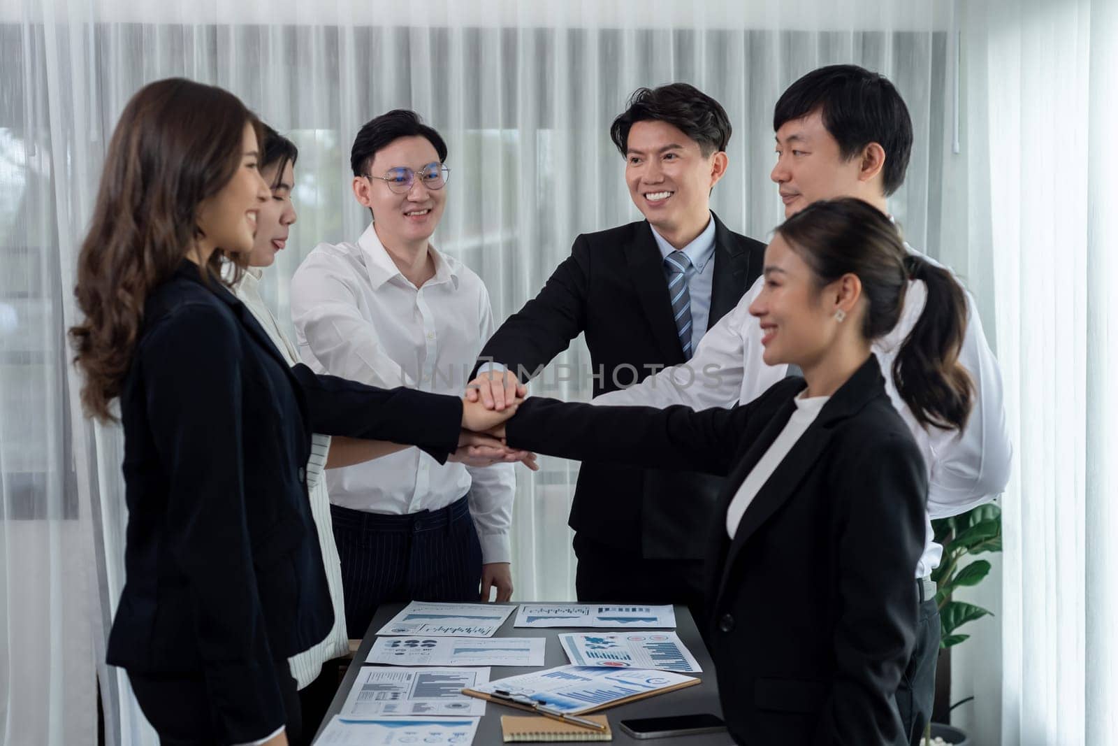 Closeup business team of suit-clad businessmen and women join hand stack together and form circle. Colleague collaborate and work together to promote harmony and teamwork concept in office workplace.