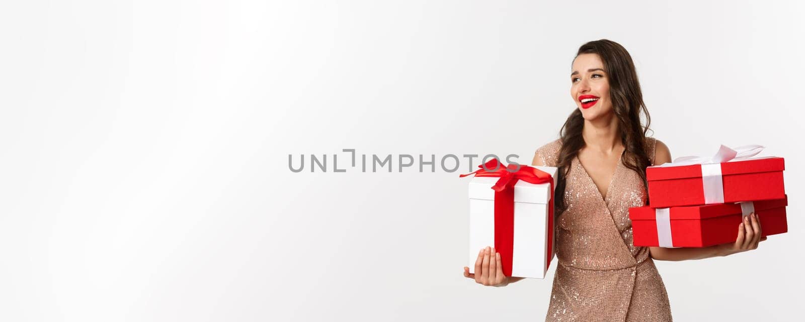 Holidays, celebration concept. Elegant woman with red lips, luxury dress, holding Christmas presents and smiling, enjoying New Year eve, white background by Benzoix