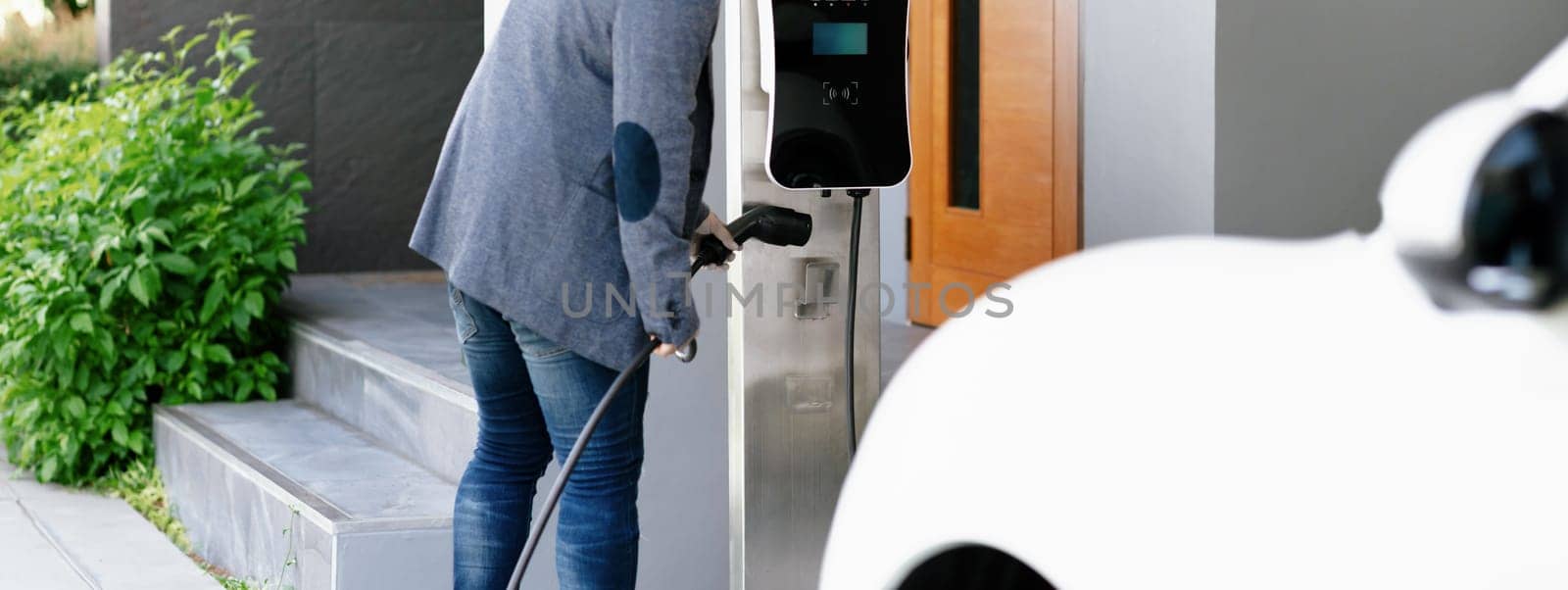 Closeup progressive asian man install cable plug to his electric car with home charging station. Concept of the use of electric vehicles in a progressive lifestyle contributes to clean environment.