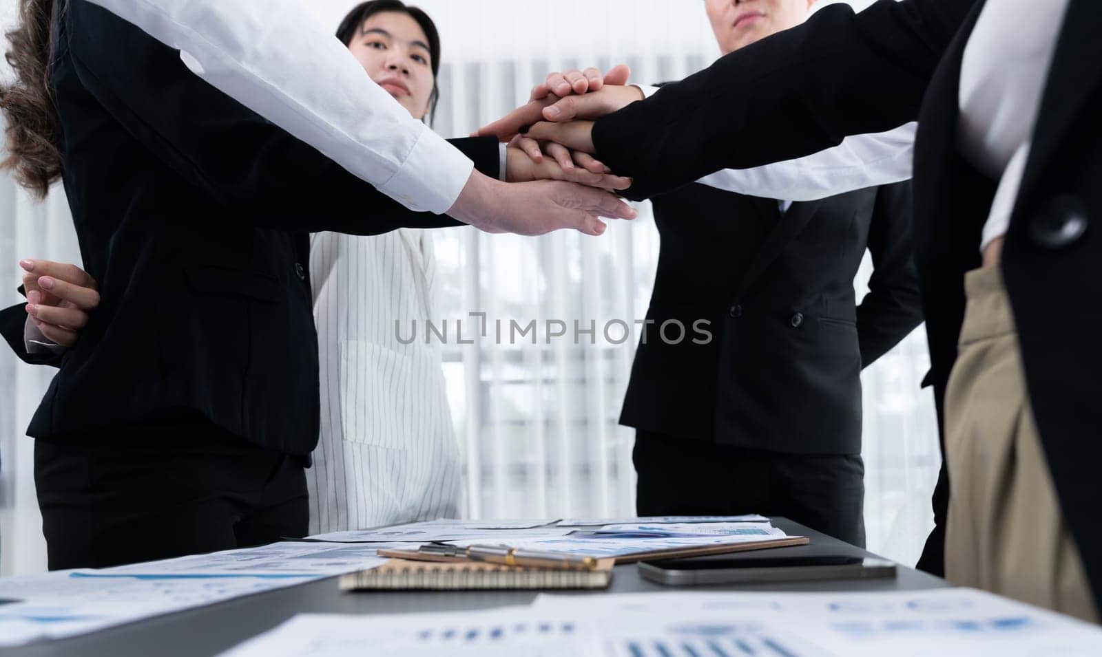 Closeup business team of suit-clad businessmen and women join hand stack together and form circle. Colleague collaborate and work together to promote harmony and teamwork concept in office workplace.