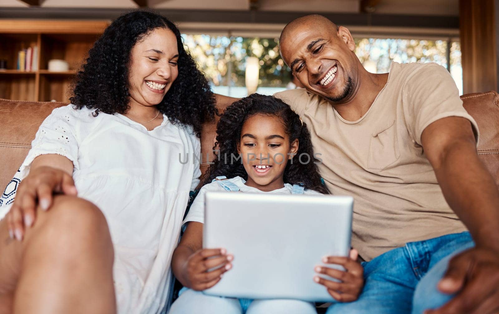 Family laughing, relax and girl with tablet on sofa in home living room for social media, funny video streaming or comic movie. Technology, smile and happy father, mother and child with touchscreen