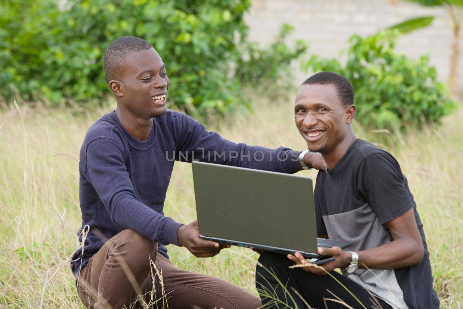 young people squatting in herbs with laptop, smiling.