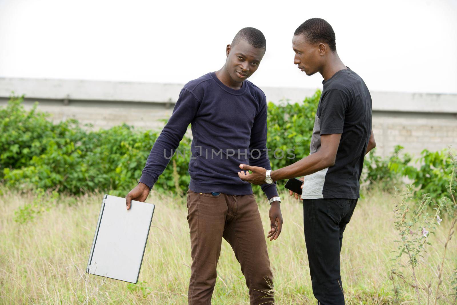 two young student arguing standing outdoors with a computer in their hands by vystek