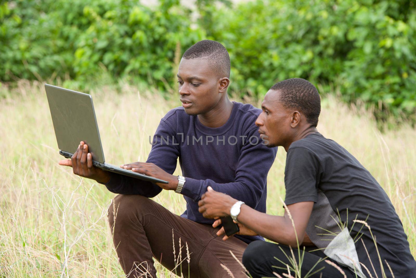 young people crouching in herbs one with laptop and both look at the screen.