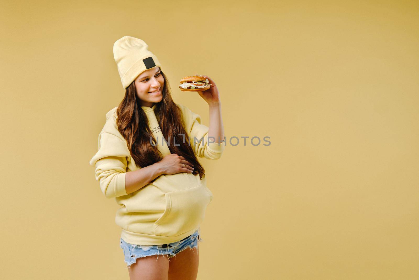 pregnant girl in yellow clothes with hamburgers in her hands on a yellow background.