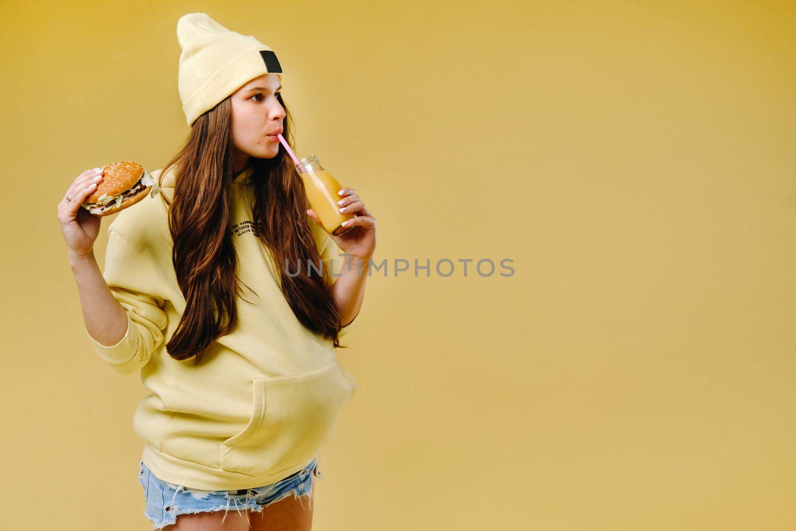 pregnant girl in yellow clothes with hamburgers in her hands on a yellow background.