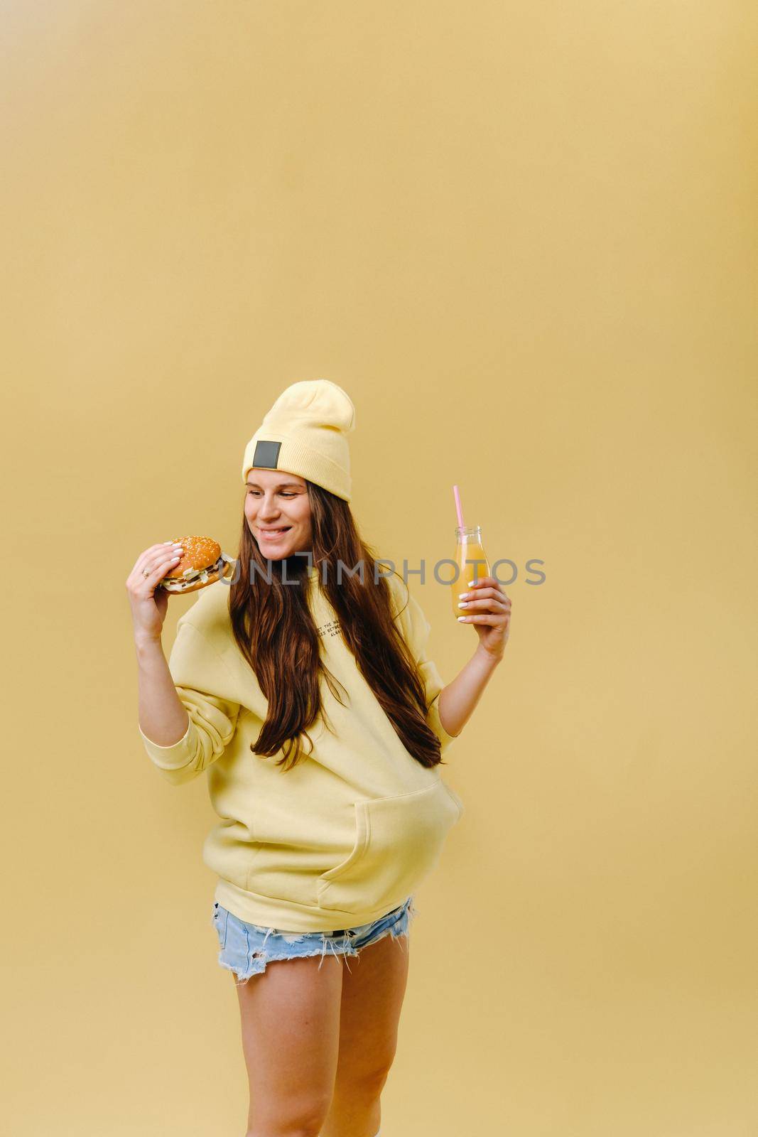 pregnant girl in yellow clothes with hamburgers in her hands on a yellow background.