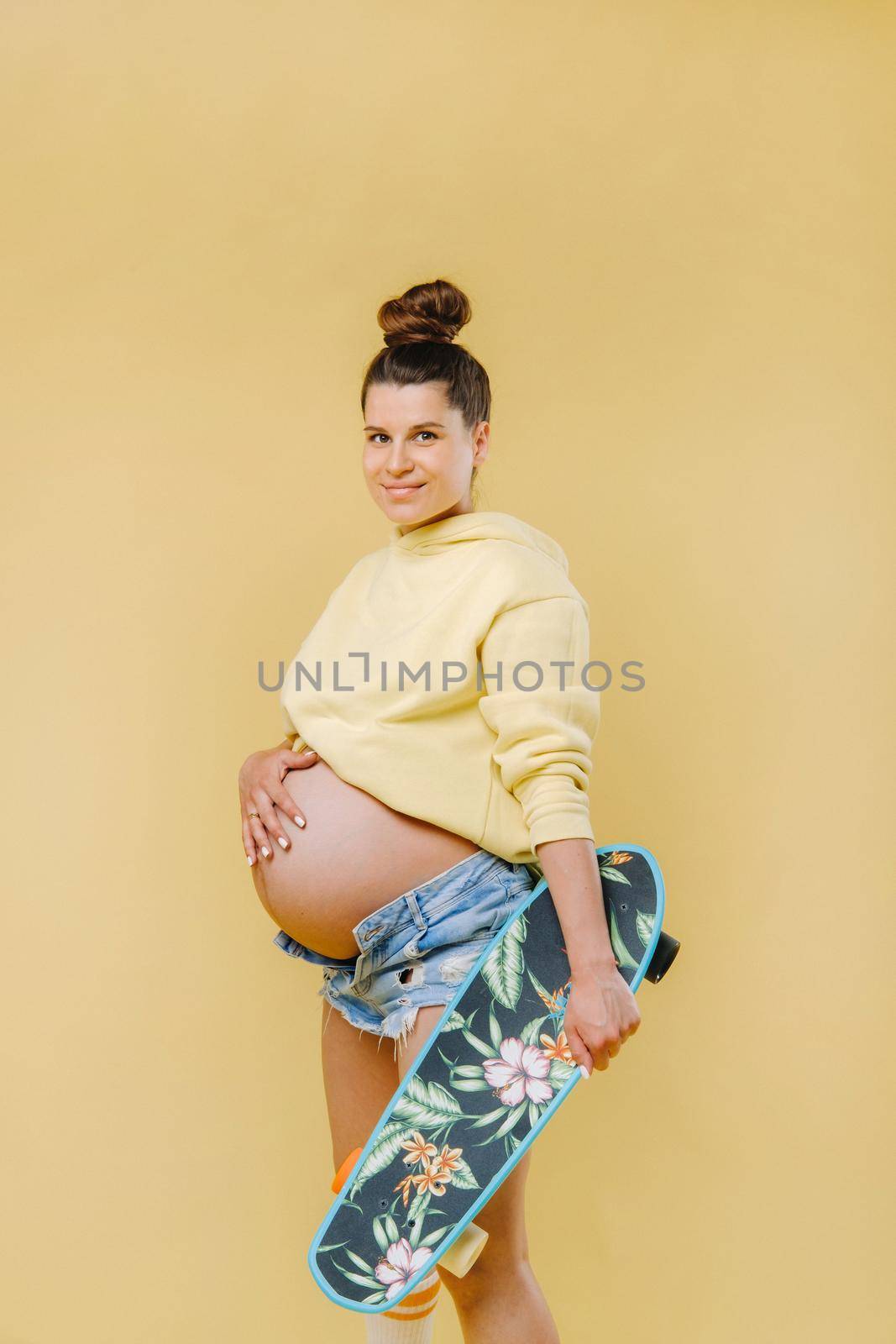 Pregnant girl in a yellow jacket with a skateboard in her hands on a yellow background by Lobachad