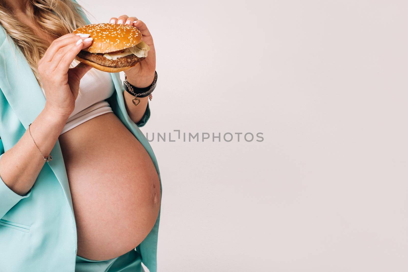 Close-up of a pregnant girl in a suit with hamburgers in her hands on a gray background.