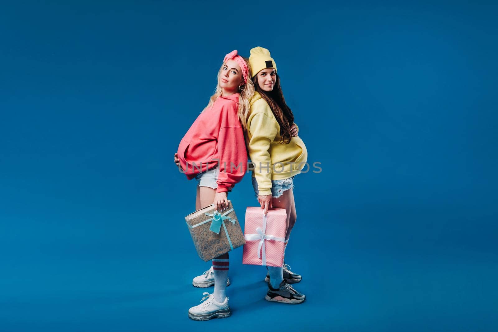 Two pregnant girls with gifts in their hands on a blue isolated background.