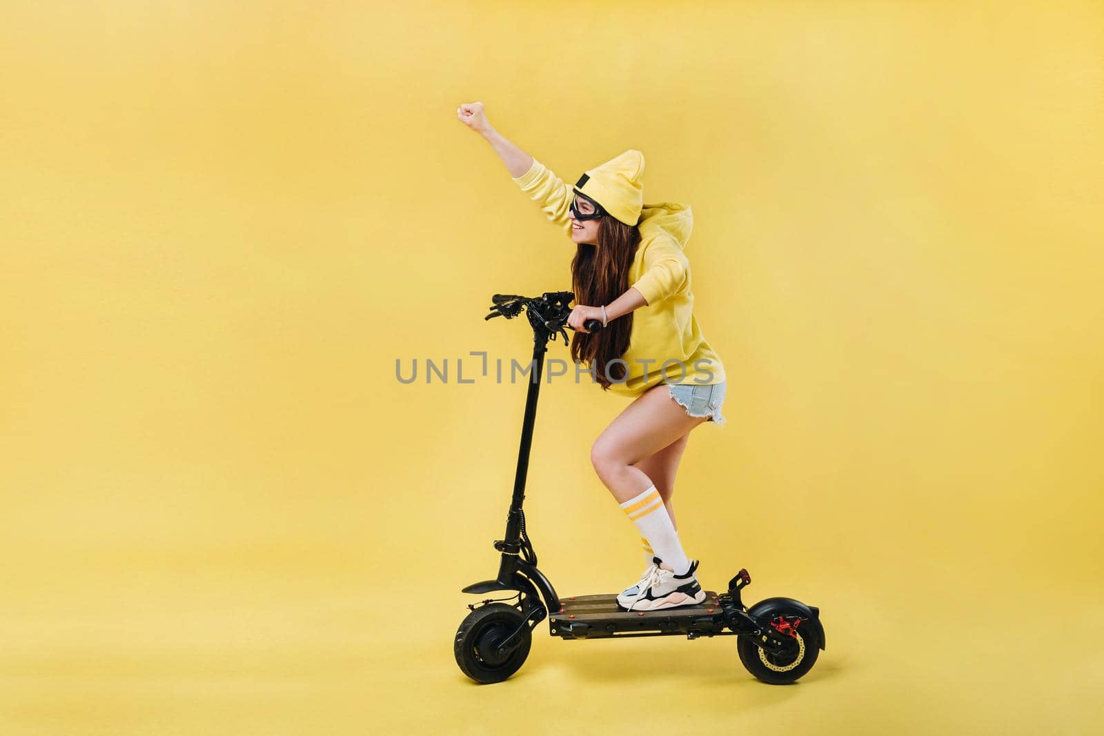 A pregnant girl in yellow clothes on an electric scooter on an isolated yellow background by Lobachad