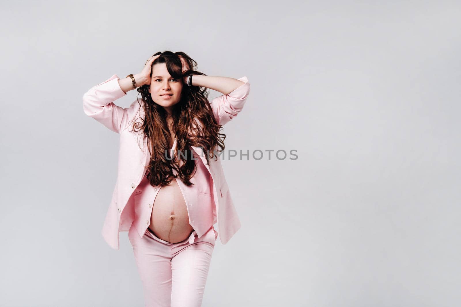 pregnant woman in pink suit close-up on gray background.